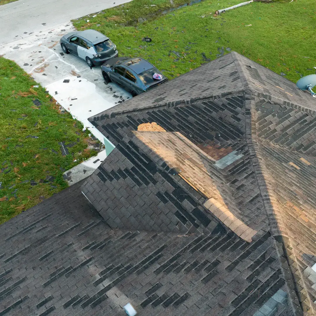 Wind damaged shingles exposing bare roof decking with shingle debris in a Houston, TX driveway
