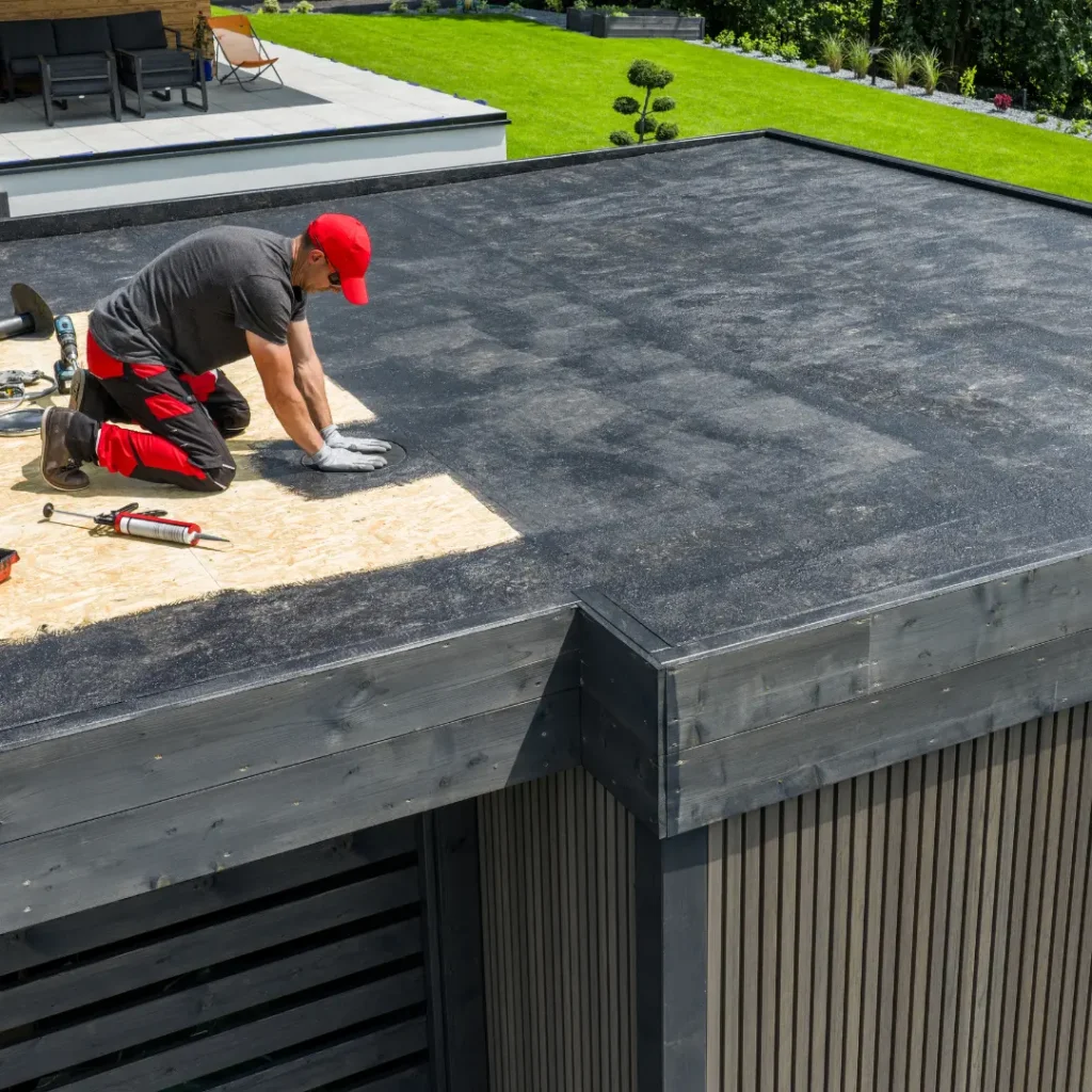 Worker installing black rubber membrane on a flat roof over plywood decking, by STX Roofing in Houston, TX